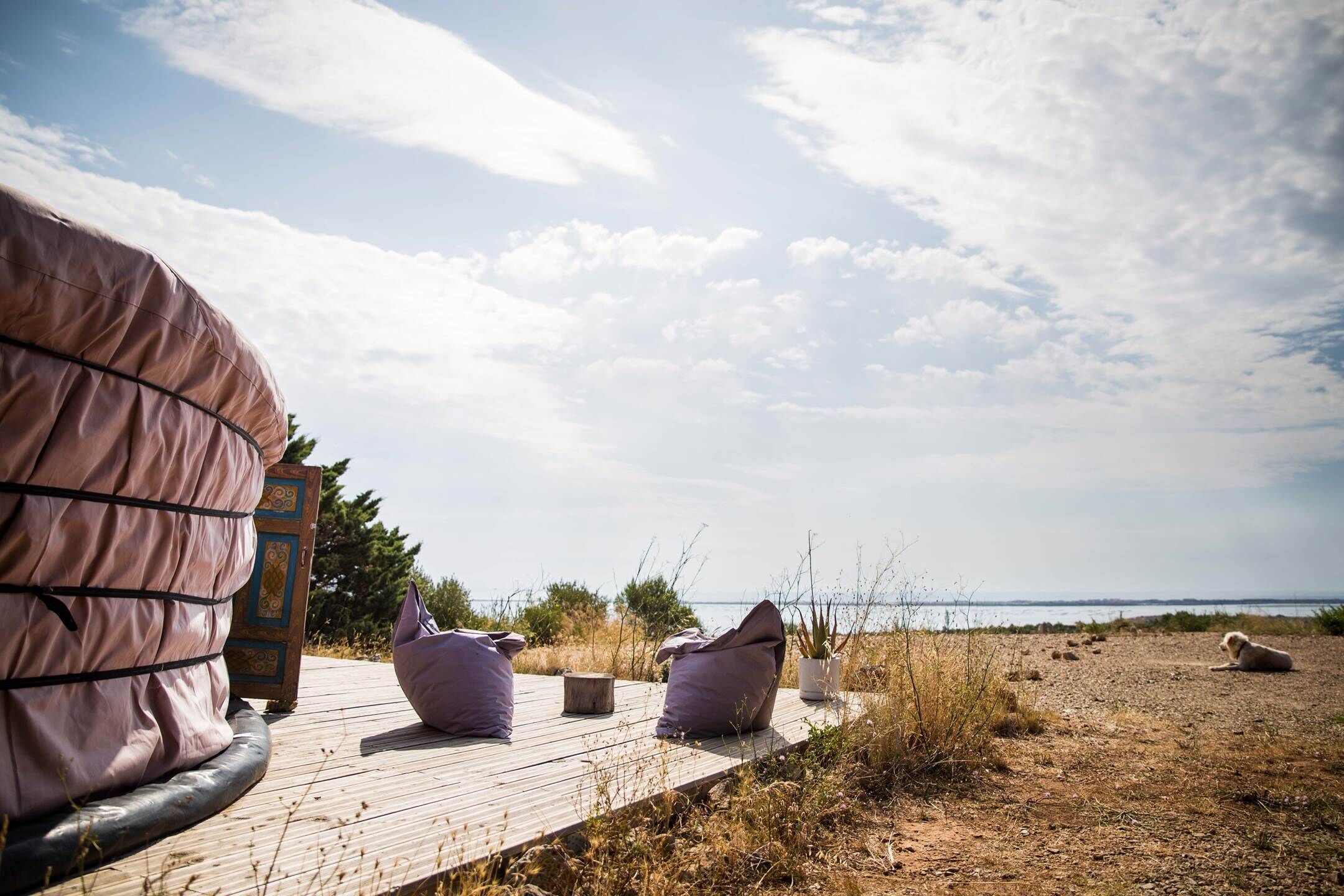 Une terrasse en bois avec une grande tente et deux fauteuils gonflables, donnant sur une plage sous un ciel dégagé.