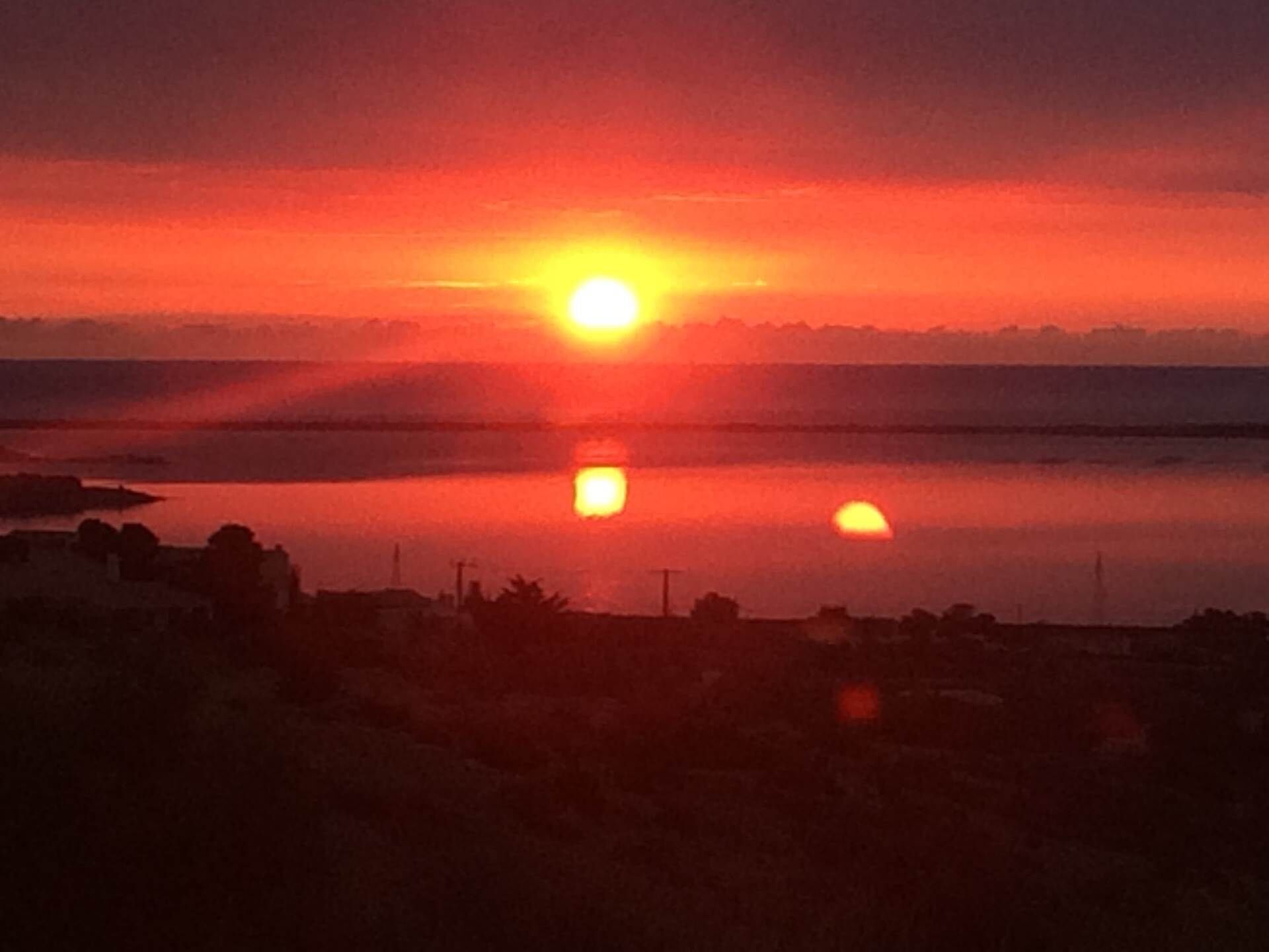 A sunset over a body of water with a silhouette of land in the foreground.