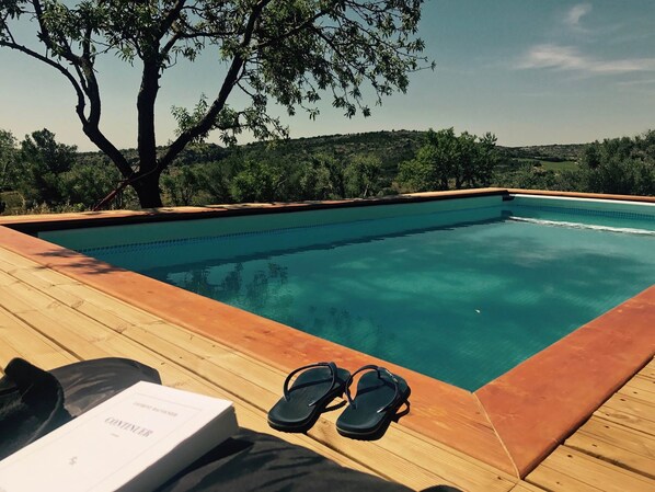Une piscine avec une terrasse en bois, une paire de tongs et un livre posé sur la terrasse.