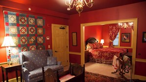 Una habitación con un sofá azul, una silla de madera, una cama con ropa de cama roja, una araña y un colcha en la pared.