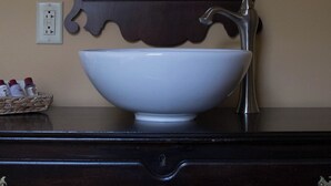 Un baño con un lavamanos blanco tipo pedestal, un mueble de tocador de madera oscura y un espejo con un marco decorativo.