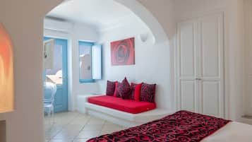 A room with a white arched doorway, a red sofa, a bed with a patterned bedspread, and a white wardrobe.