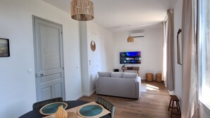 Zona pranzo con tavolo apparecchiato per quattro persone, divano sullo sfondo e televisore a parete.