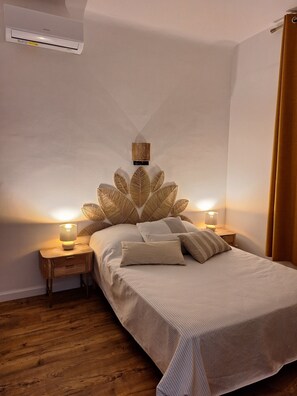 Ein Schlafzimmer mit einem Bett, Nachttischlampen, einer Wandklimaanlage und Holzboden.
