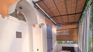 Un'area patio coperta con tavolo e sedie, una pianta in vaso e un lampadario a parete.