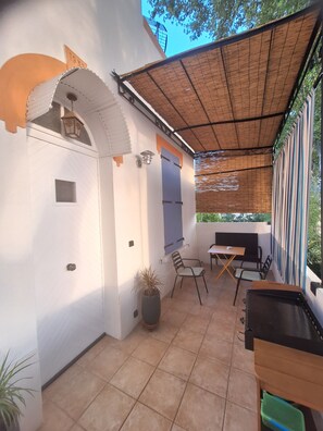 Ein überdachter Patio-Bereich mit Tisch, Stühlen, einer Topfpflanze und einer wandmontierten Leuchte.