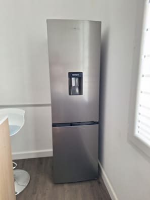 Ein Edelstahl-Kühlschrank mit Wasserspender in einem Raum mit Holzboden und weißen Wänden.