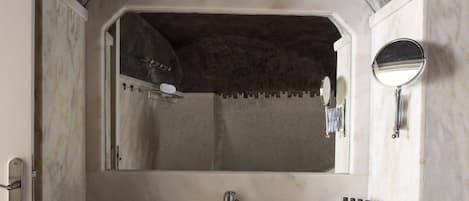 A bathroom with a large mirror, a sink, and a shower area.
