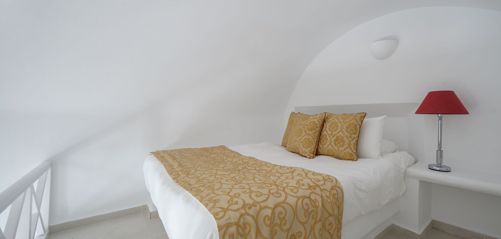 Un lit avec une couvre-lit à motifs, deux oreillers, une lampe rouge et un mur blanc.
