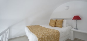 Un lit avec une couvre-lit à motifs, deux oreillers, une lampe rouge et un mur blanc.