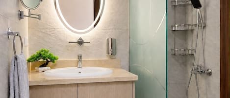 A modern bathroom with a round mirror, a sink, a small plant, and a glass shower enclosure.