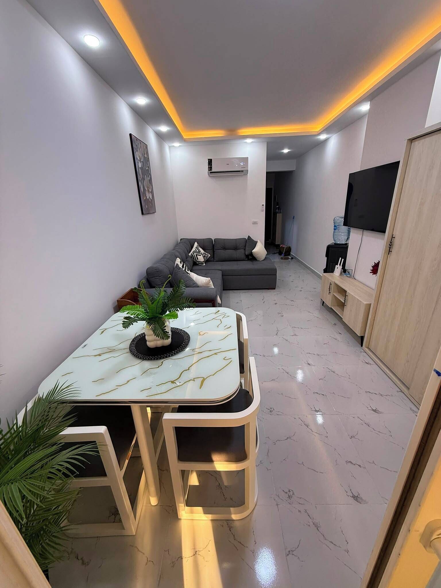 Una sala de estar moderna con un sofá seccional, una mesa de comedor con sillas, un televisor de pantalla plana y un equipo de aire acondicionado.