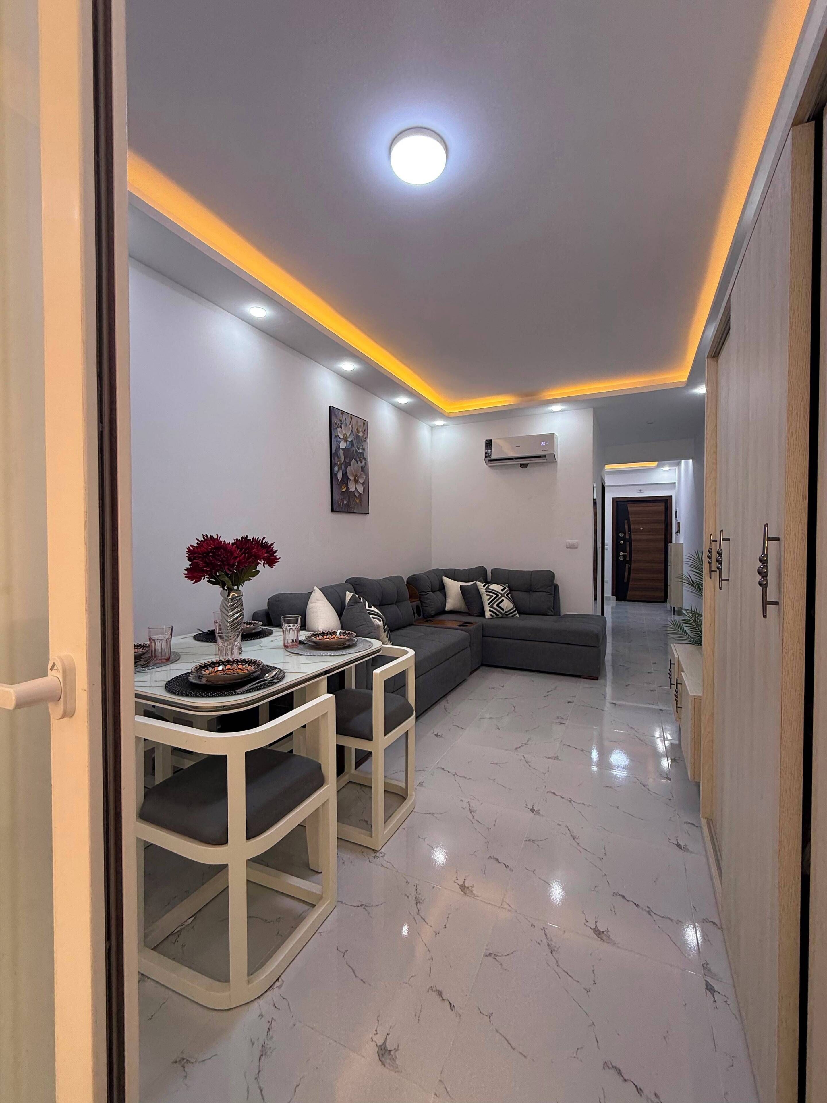 A modern living room with a sectional sofa, a dining table with chairs, and a marble floor.