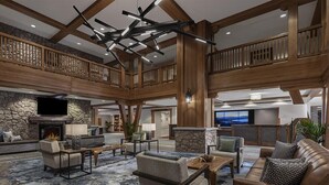 Eine geräumige Lobby mit Kamin aus Stein, mehreren Sitzbereichen und einer hohen Decke mit freiliegenden Balken.