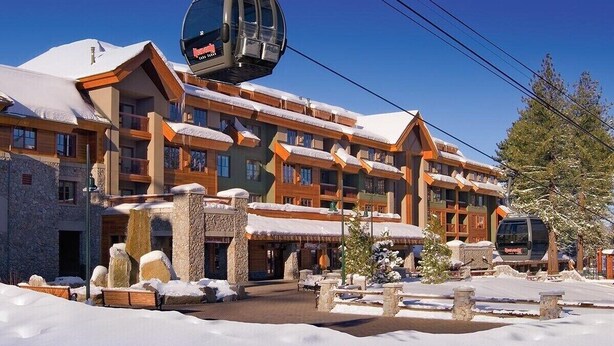 Ein mehrstöckiges Hotel mit Skilift, Steinsäulen und verschneiter Umgebung.