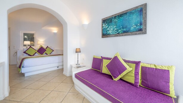 A hotel room with a bed, a sofa, a painting, and a lamp. - Lioren Suite, Divine Sea Views, Santorini (Santorini)