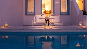 A poolside seating area with a table, two chairs, and two lit lanterns. - Lioren Suite, Divine Sea Views, Santorini (Santorini)