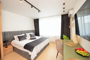 Quarto de hotel moderno com uma cama grande, mesas de cabeceira, uma escrivaninha com cadeira e uma cesta de frutas.