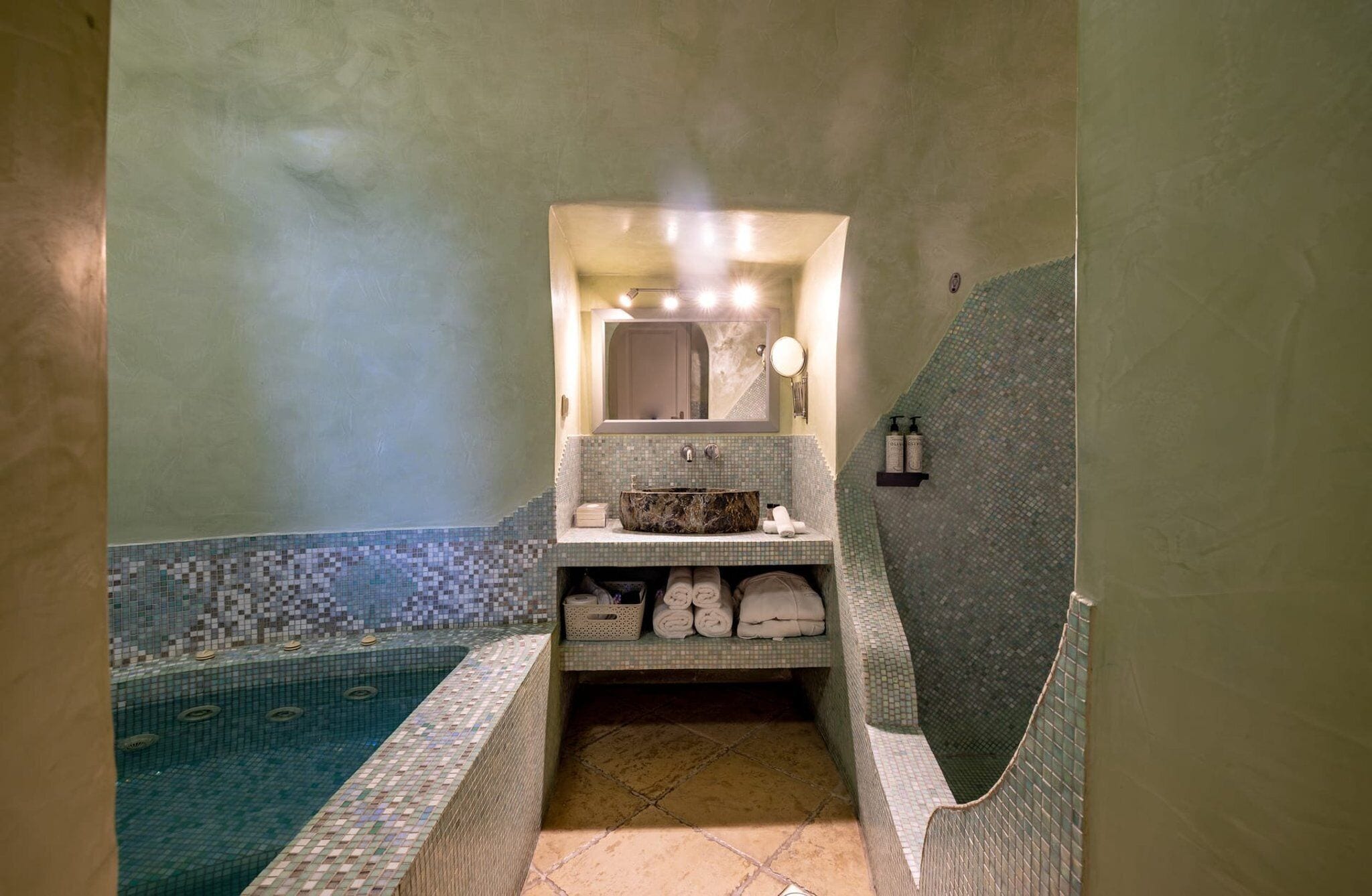 Une salle de bain avec un sol carrelé, un lavabo avec un miroir et une baignoire.