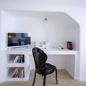 A white desk with a computer, speakers, and a coffee machine. A black chair is in front of the desk. Books are on a shelf below the desk. - Elysora Suite, Divine Sea Views, Outdoor & Indoor Jacuzzi, Santorini (Santorini)