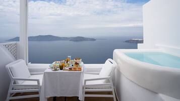 A balcony with white furniture, a table with food, and a hot tub.