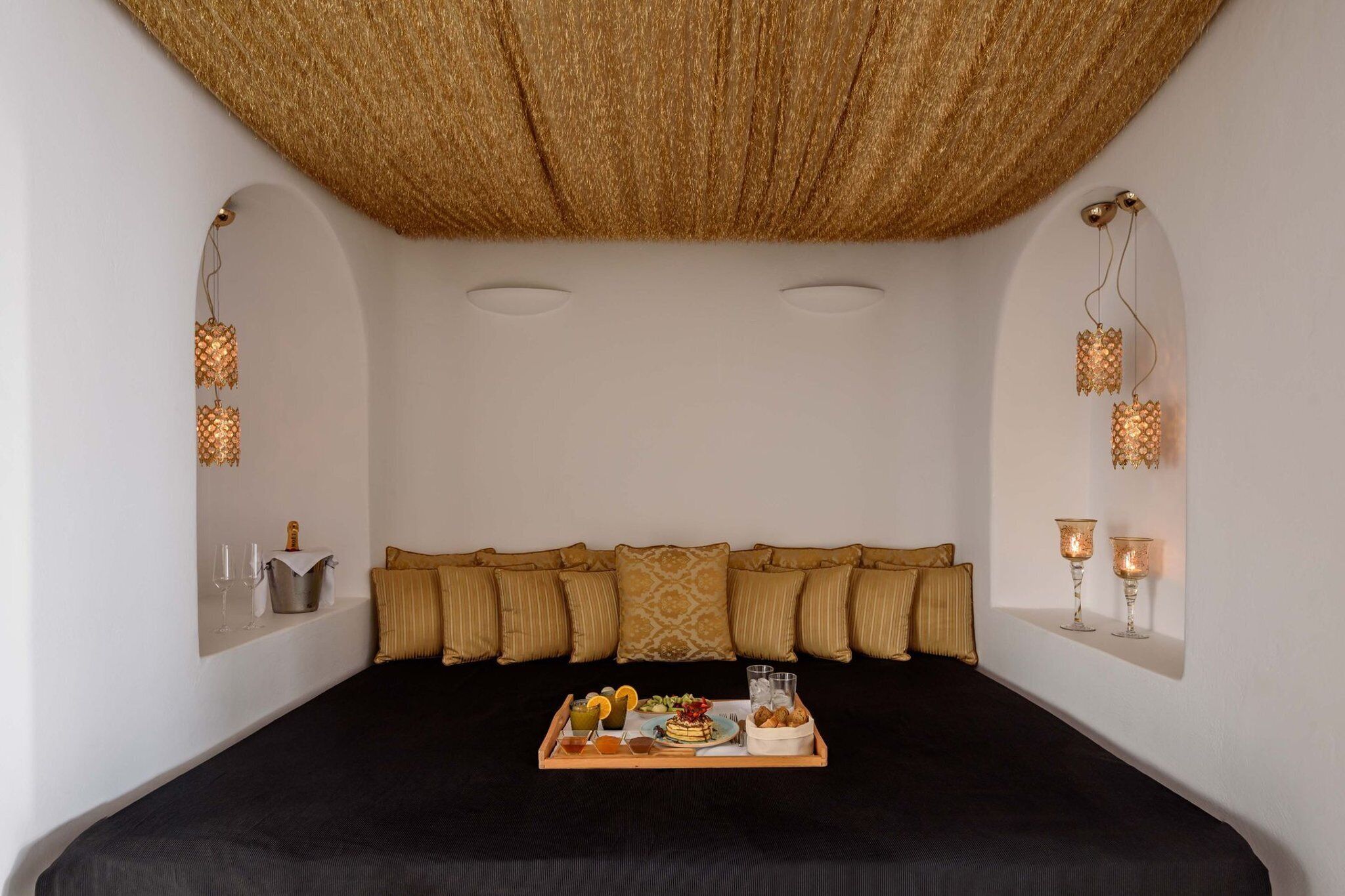 Een slaapkamer met een bed, kussens, een dienblad met eten en drinken, en wandlampen.