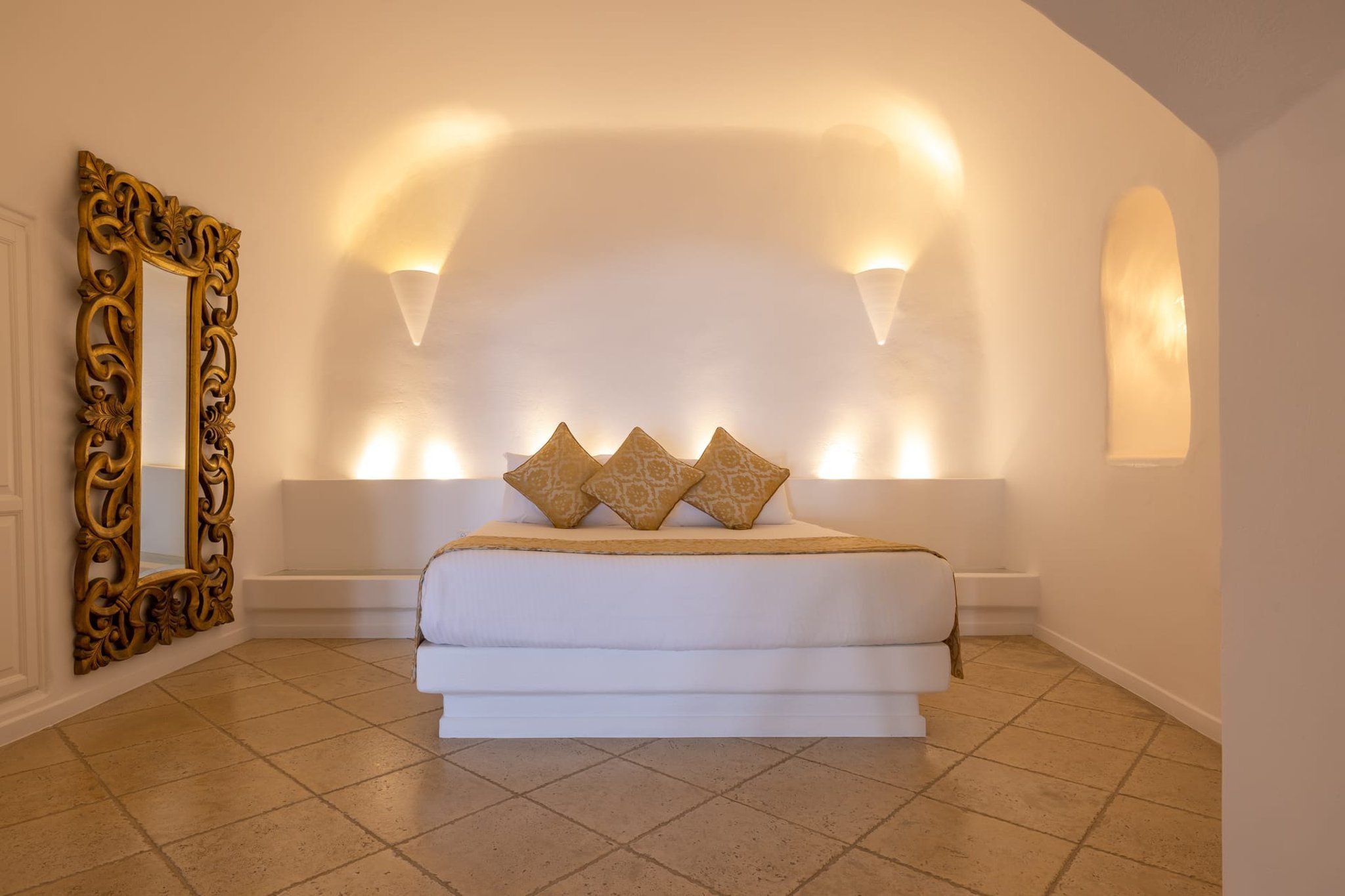 A bedroom with a large bed, a decorative mirror, and wall-mounted lighting.