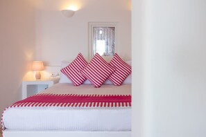 Ein Bett mit rot-weiß gestreifter Bettwäsche, eine Nachttischlampe und ein Fenster mit Vorhang.