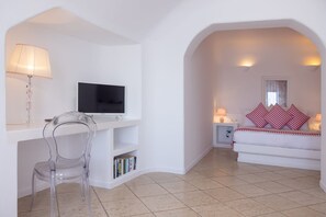 Ein Zimmer mit Fernseher, Schreibtisch, Sessel, Sofa und Fenster.