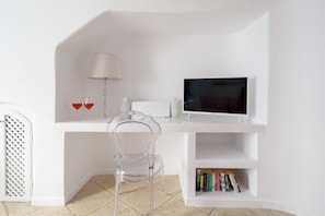 Ein weißer Schreibtisch mit transparentem Stuhl, einem Fernseher, einer Lampe und einem Bücherregal.