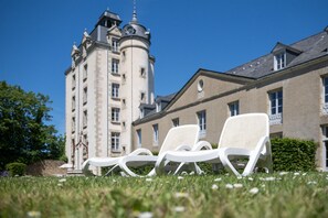 Un edificio con una torre, dos sillones blancos y un césped cuidado.