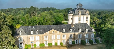 Ein großes, historisches Gebäude mit zahlreichen Fenstern und einem markanten Turm, umgeben von üppigem Grün.