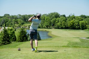 A golfer on a golf course with a lake and trees in the background.