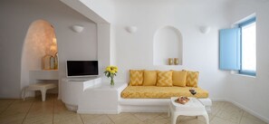 A modern living room with a sofa, TV, small table, and decorative items. - Coralyon Suite, Divine Sea Views, Outdoor Jacuzzi, Santorini (Santorini)