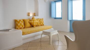 A room with a sofa, a small table, and a chair. There are two windows with blue shutters and a door with a blue frame.