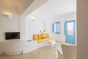A modern living room with a flat-screen TV, a white sofa with yellow cushions, a white coffee table, and a blue door. - Coralyon Suite, Divine Sea Views, Outdoor Jacuzzi, Santorini (Santorini)
