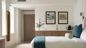 Una habitación de hotel con una cama, una mesita de noche, un espejo, un lavabo y dos cuadros enmarcados en la pared.