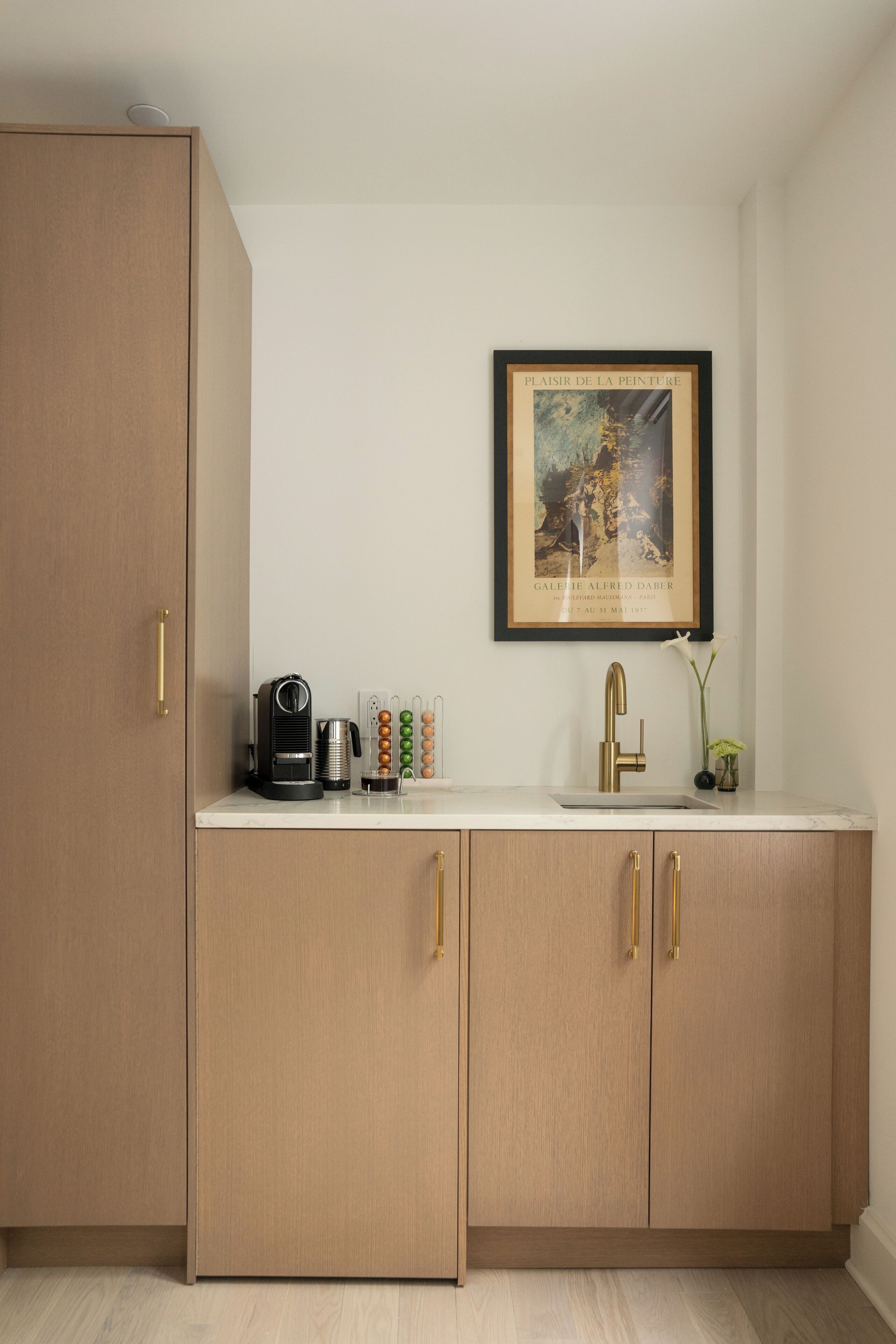 A kitchen with wooden cabinets, a coffee machine, a sink, and a framed artwork on the wall.