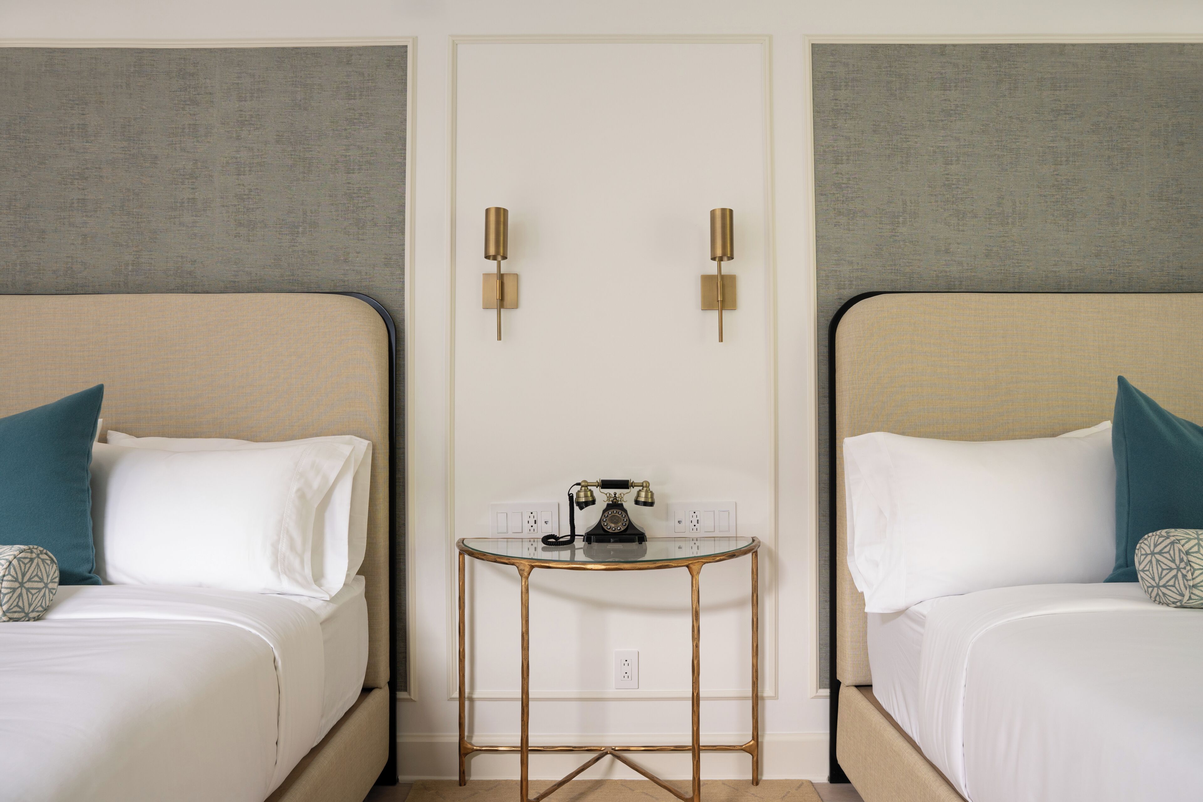 Une chambre d’hôtel avec deux lits, une petite table avec un téléphone et des lampes fixées au mur.