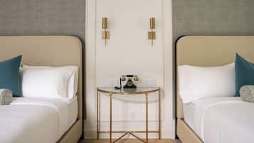 A hotel room with two beds, a small table with a telephone, and wall-mounted light fixtures.