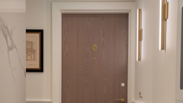 Un pasillo con puerta de madera, un cuadro enmarcado en la pared y suelo de mármol.