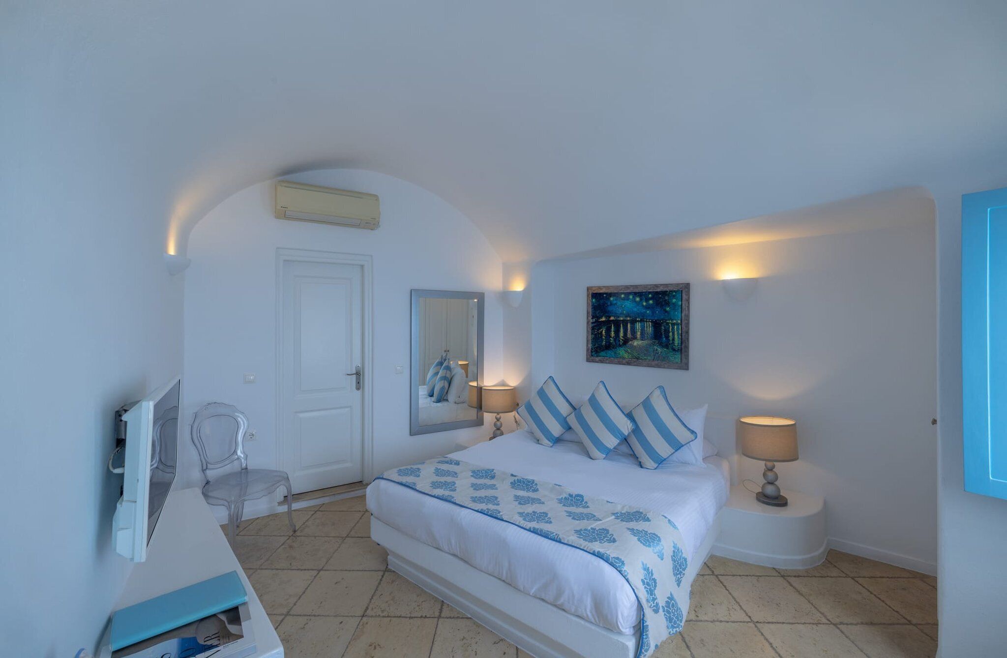 Une chambre à coucher avec un lit, des lampes de chevet, une chaise, un bureau, un miroir et un tableau accroché au mur.