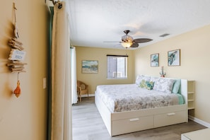 A bedroom with a bed, a ceiling fan, a window with blinds, and artwork on the walls.
