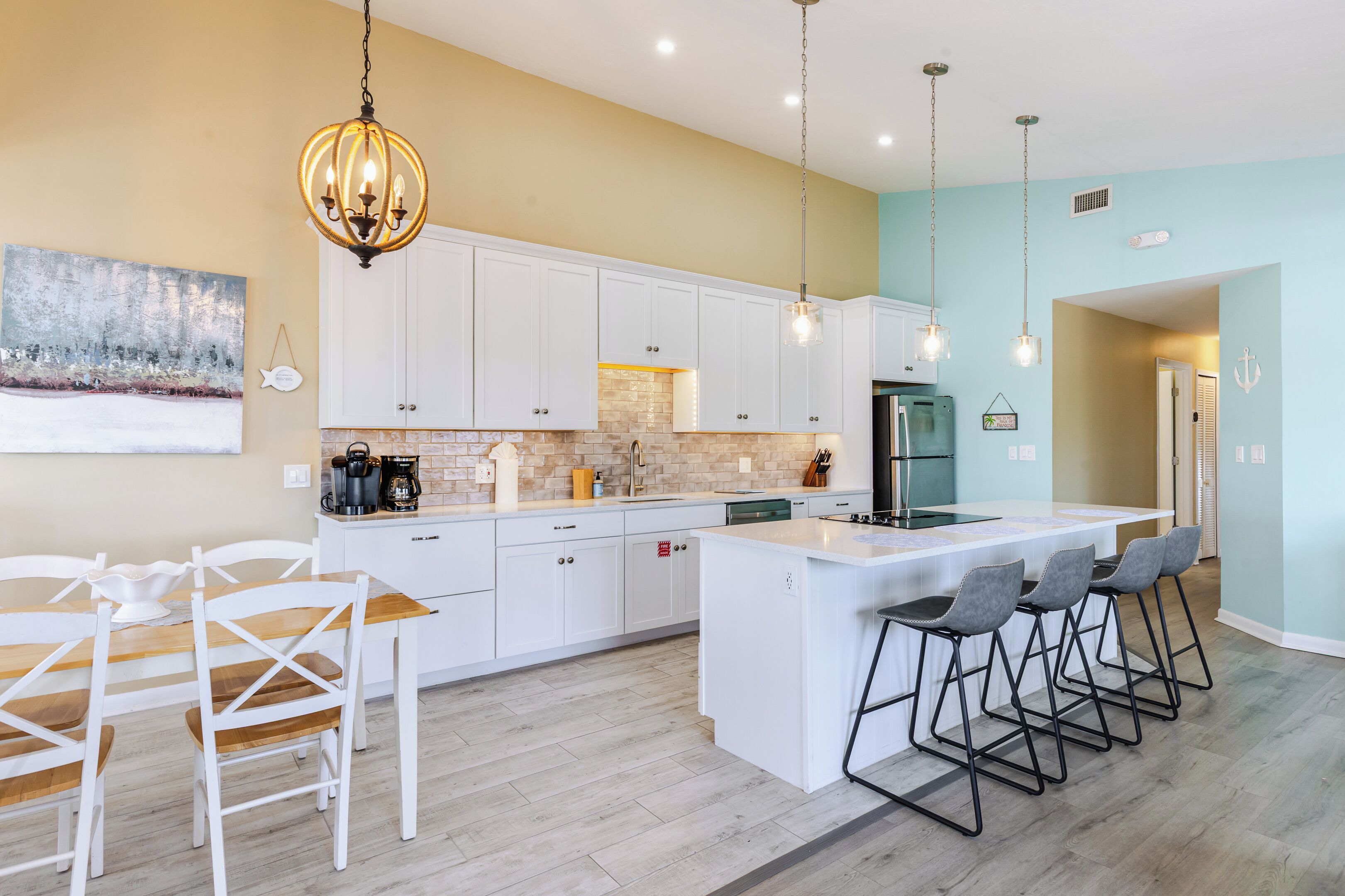 A modern kitchen with white cabinets, a central island, bar stools, and pendant lighting.