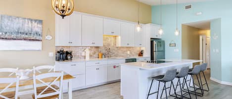 A modern kitchen with white cabinets, a central island, bar stools, and pendant lighting.