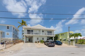 Ein Strandhotel mit Balkon, überdachtem Parkplatz und Kiesweg.