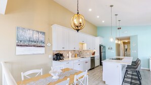 Une cuisine moderne avec des meubles blancs, un îlot central, des tabourets de bar et des luminaires suspendus.