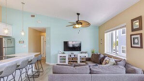 Un salon moderne avec un canapé d’angle gris, un téléviseur à écran plat et un ventilateur de plafond.