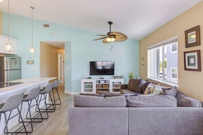 Ein modernes Wohnzimmer mit einem grauen Ecksofa, einem Flachbildfernseher und einem Deckenventilator.