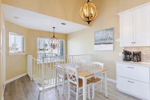 A dining area with a wooden table, white chairs, a chandelier, and a view of the outdoors through large windows. - CHARMING KCB CANAL FRONT 3 BEDROOM DUPLEX WITH CABANA CLUB - POOL & BEACH ACCESS (Marathon)